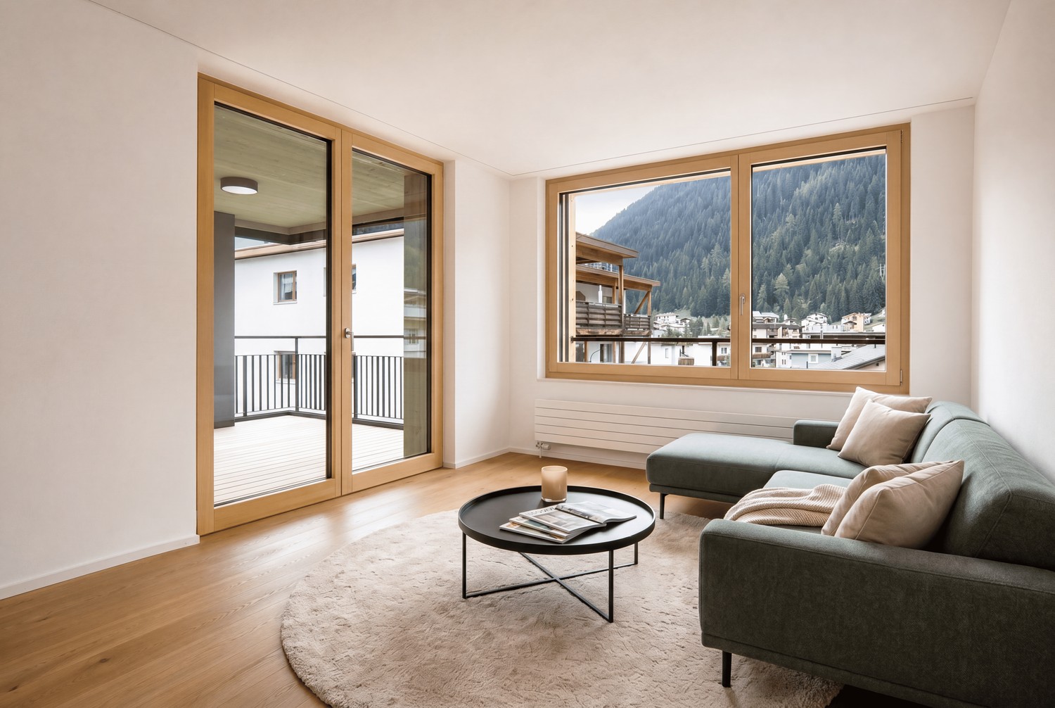 Heller Wohnbereich mit Eichenparkett, grossen Holzfenstern, grauem Ecksofa und Zugang zum Balkon.