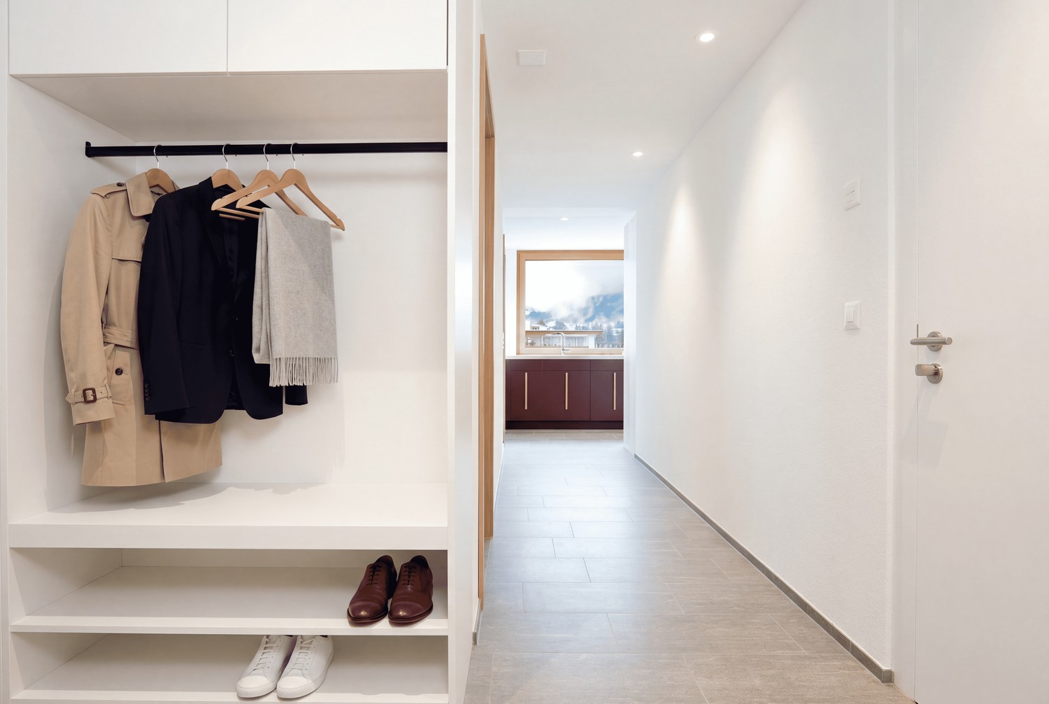 Moderner Eingangsbereich mit weisser Einbaugarderobe, offenen Schuhregalen und hellem Flur mit grauem Fliesenboden.