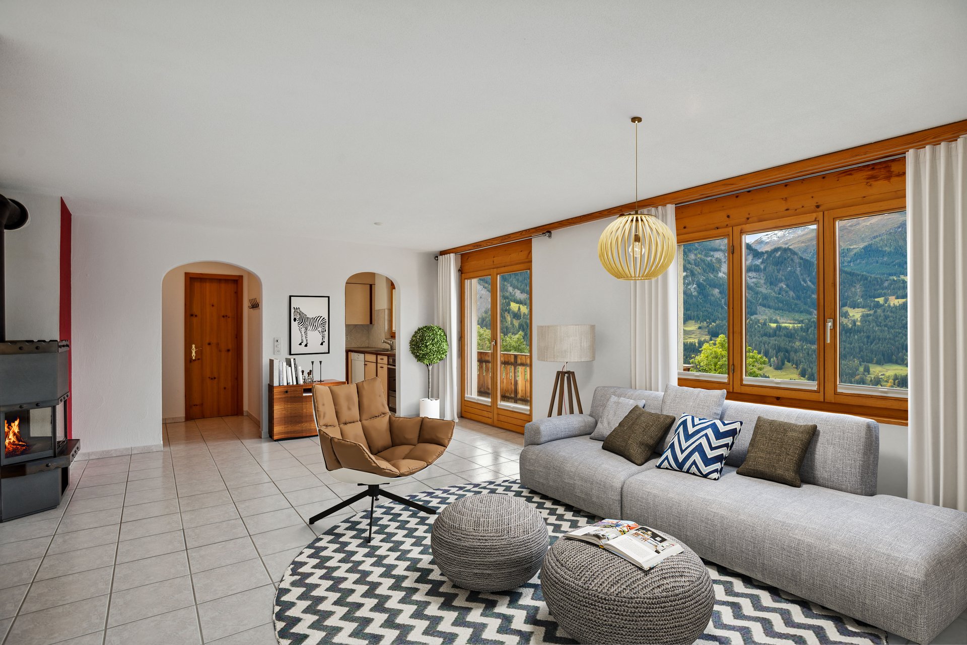 Heller Wohnbereich mit grossen Holzfenstern, gemütlicher Sitzecke, Kamin und beeindruckendem Blick auf die Berglandschaft.