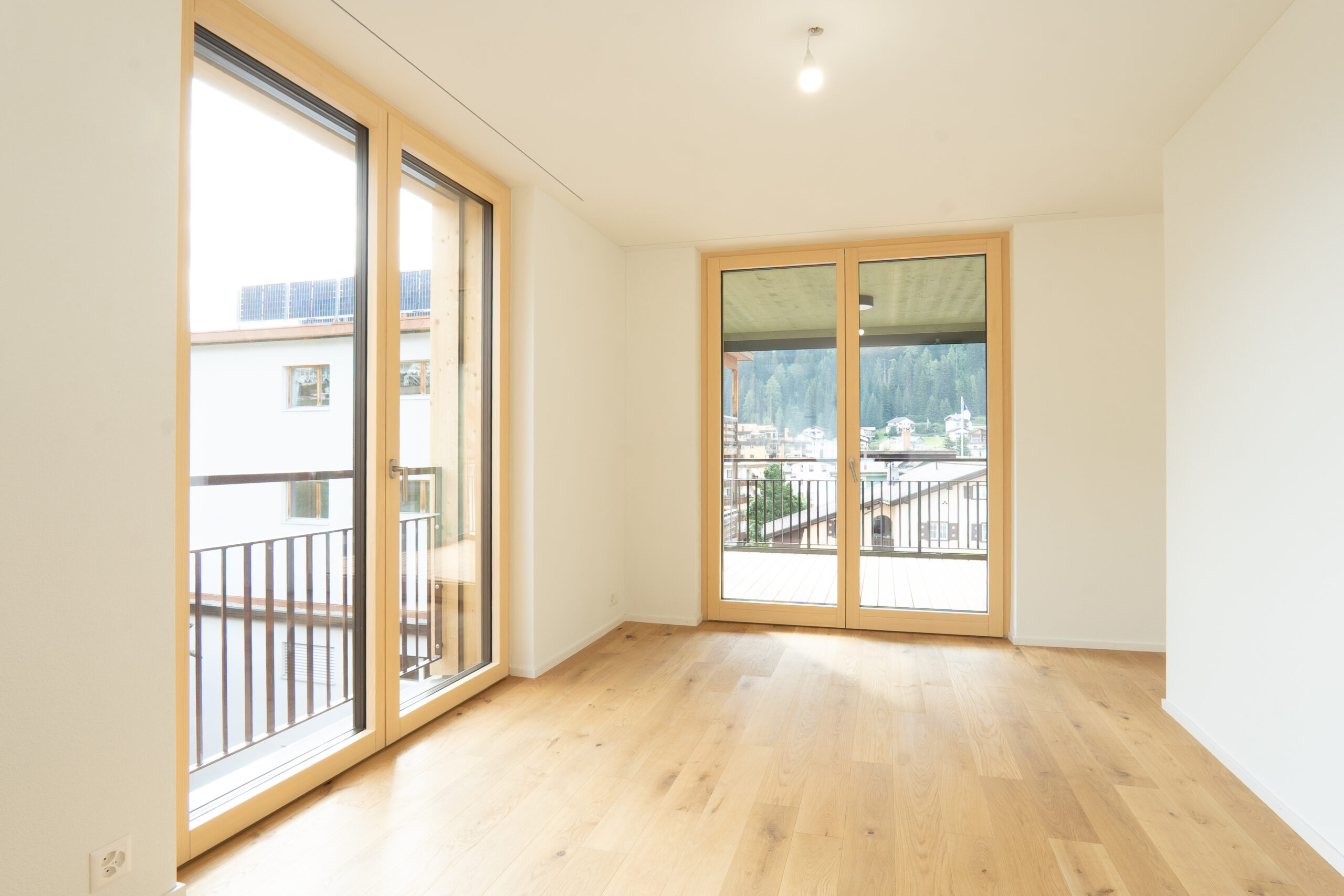 Lichtdurchfluteter Wohnraum mit natürlichem Eichenparkett und grosszügigen Holzfenstertüren zum Balkon.