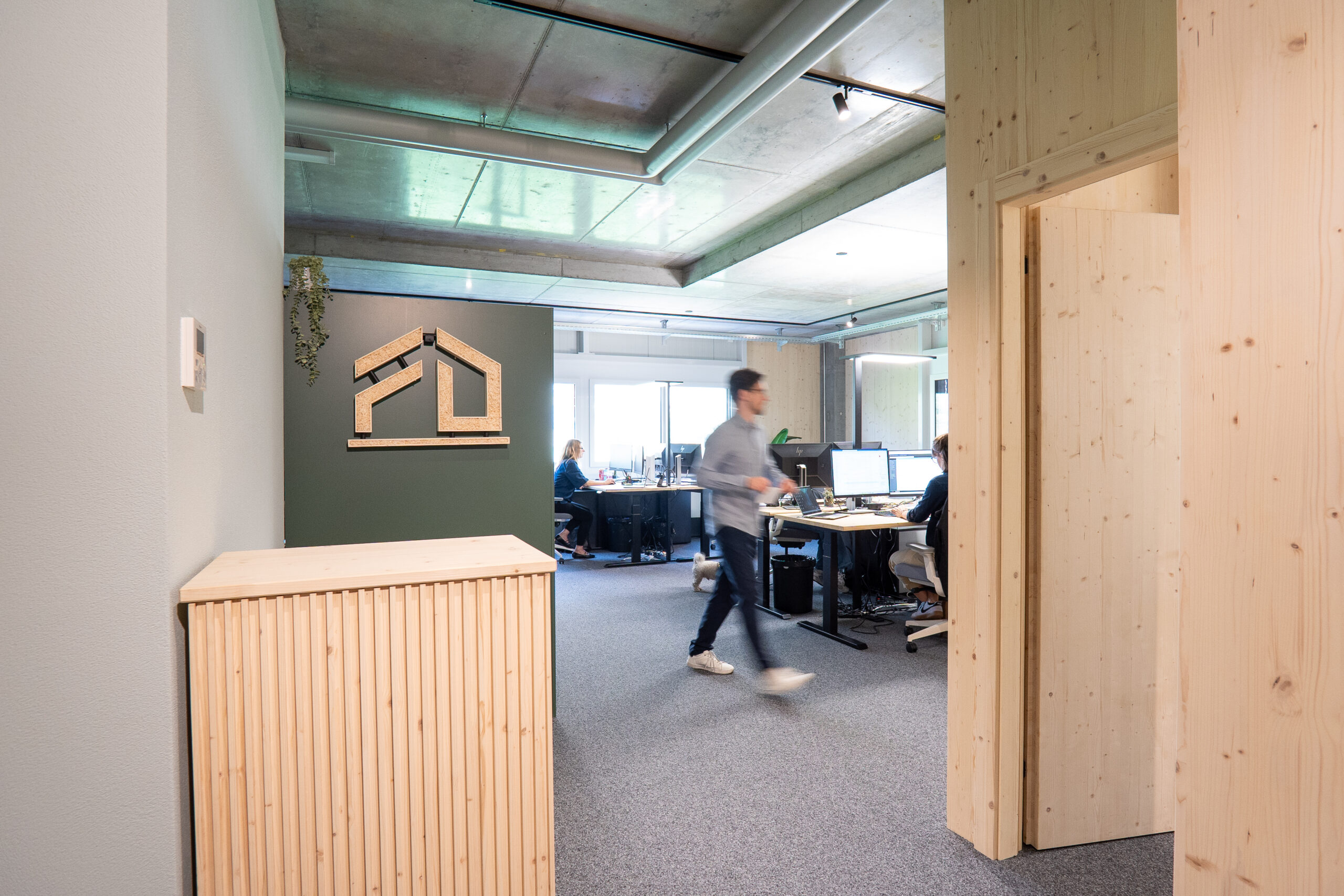 Offener Bürobereich der Deflorin AG mit Holzelementen, modernen Arbeitsplätzen und Mitarbeitenden bei der Arbeit.