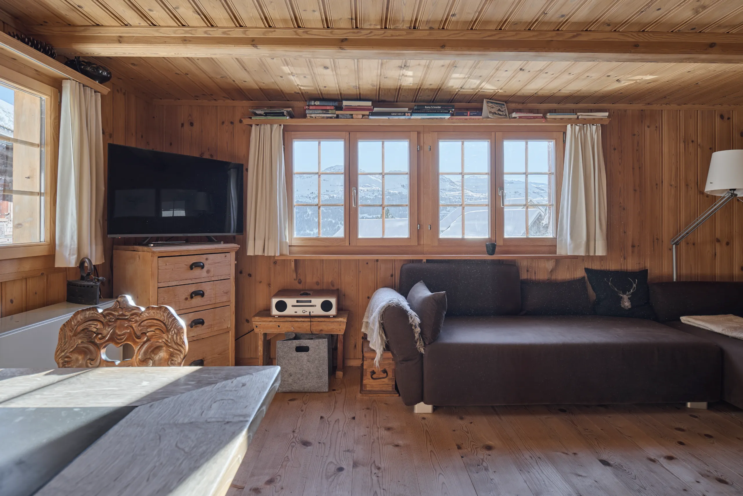 Gemütlicher Wohnbereich im Ferienhaus Siat mit Holzverkleidung, Holzboden, dunklem Sofa und Bergblick.