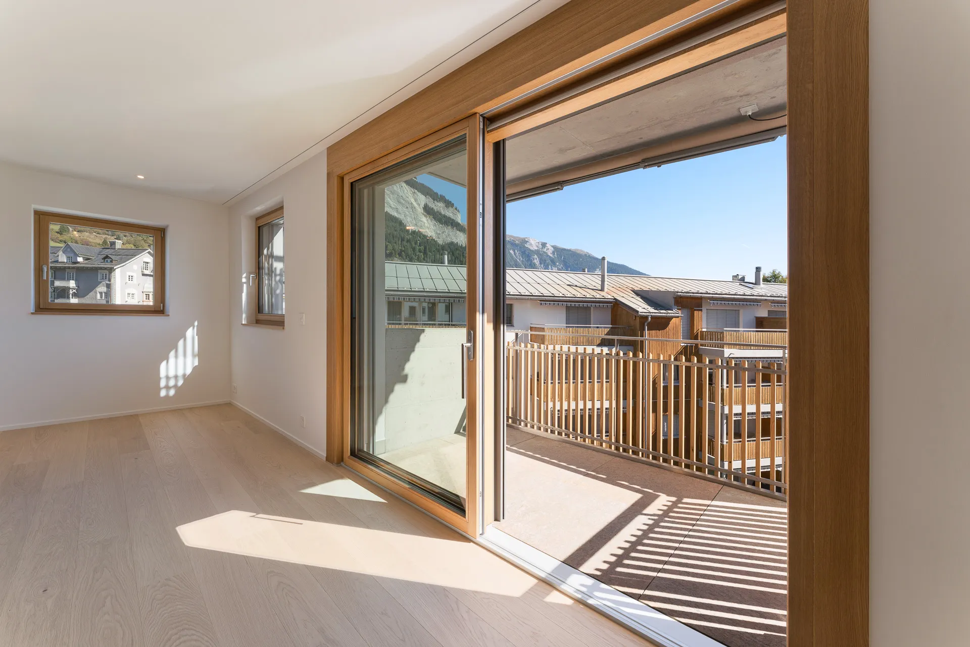 Sonnendurchfluteter Wohnraum in Flims Dorf mit Eichenparkett, grossen Holzschiebetüren und direktem Balkonzugang.