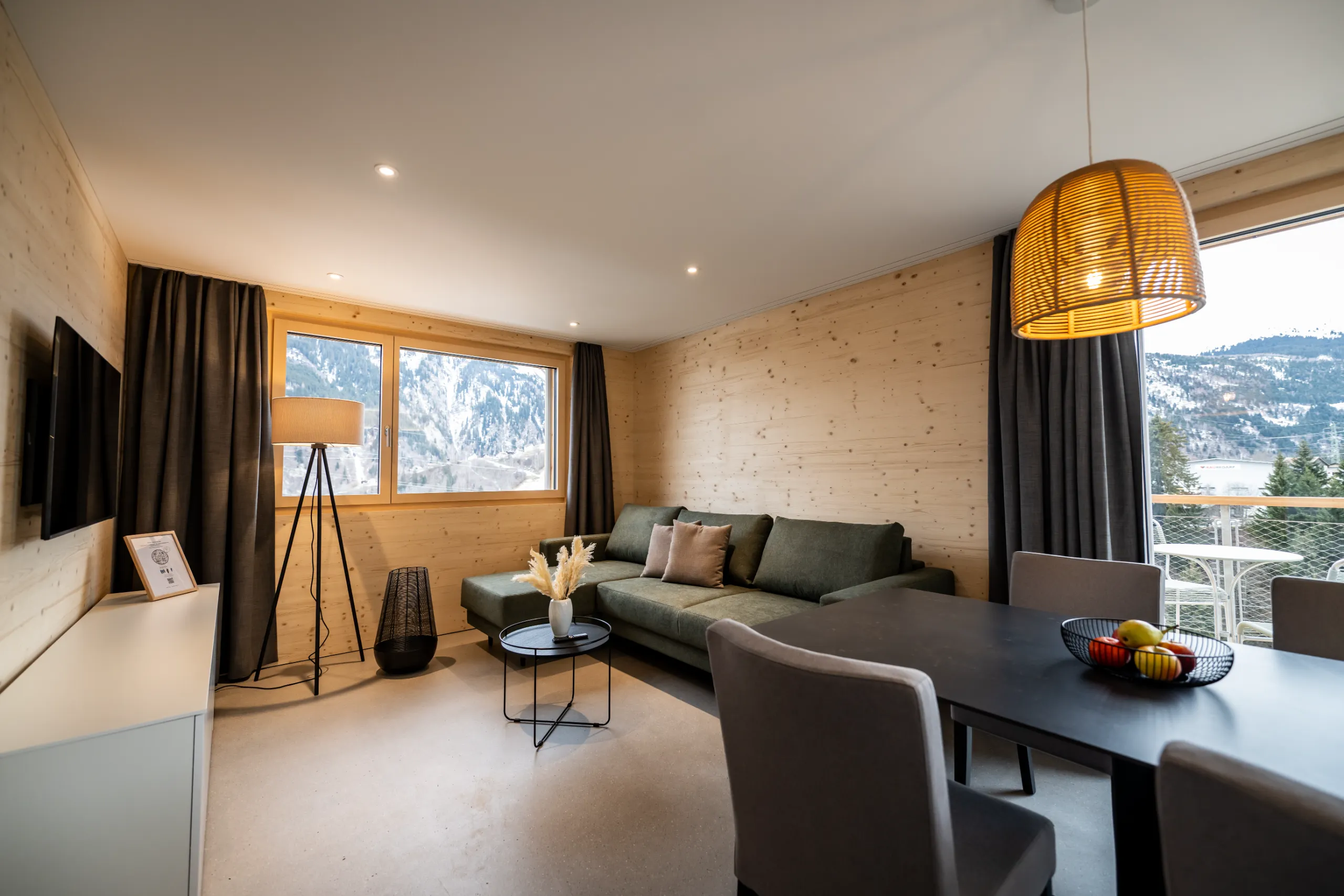 Gemütlicher Wohnbereich der Residenza Pazzola mit Holzverkleidung, grünem Sofa, Essbereich und Bergblick.