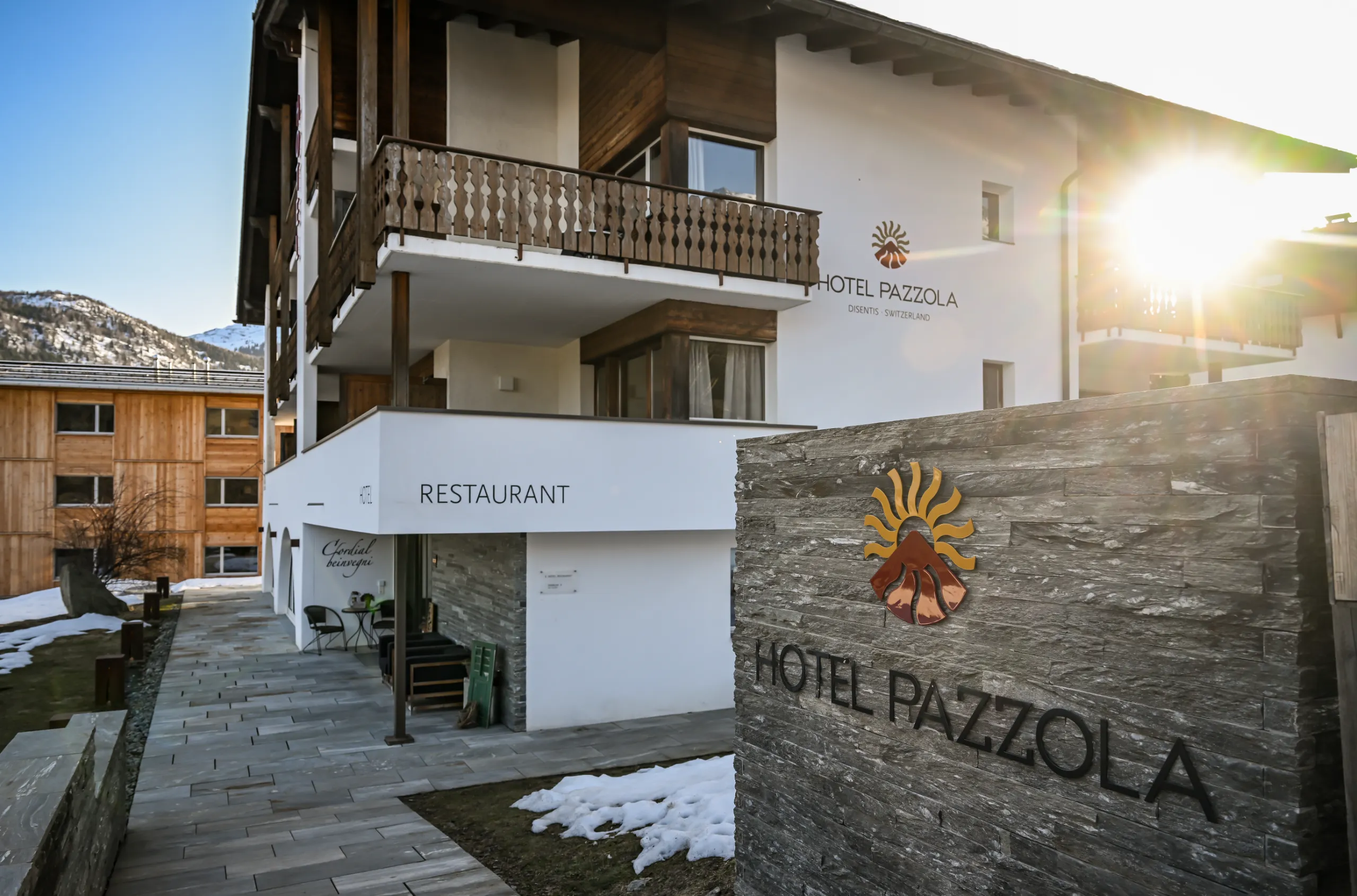 Aussenansicht der Residenza Pazzola in Disentis/Mustér mit traditionellen Holzbalkonen und Restaurant im Erdgeschoss.