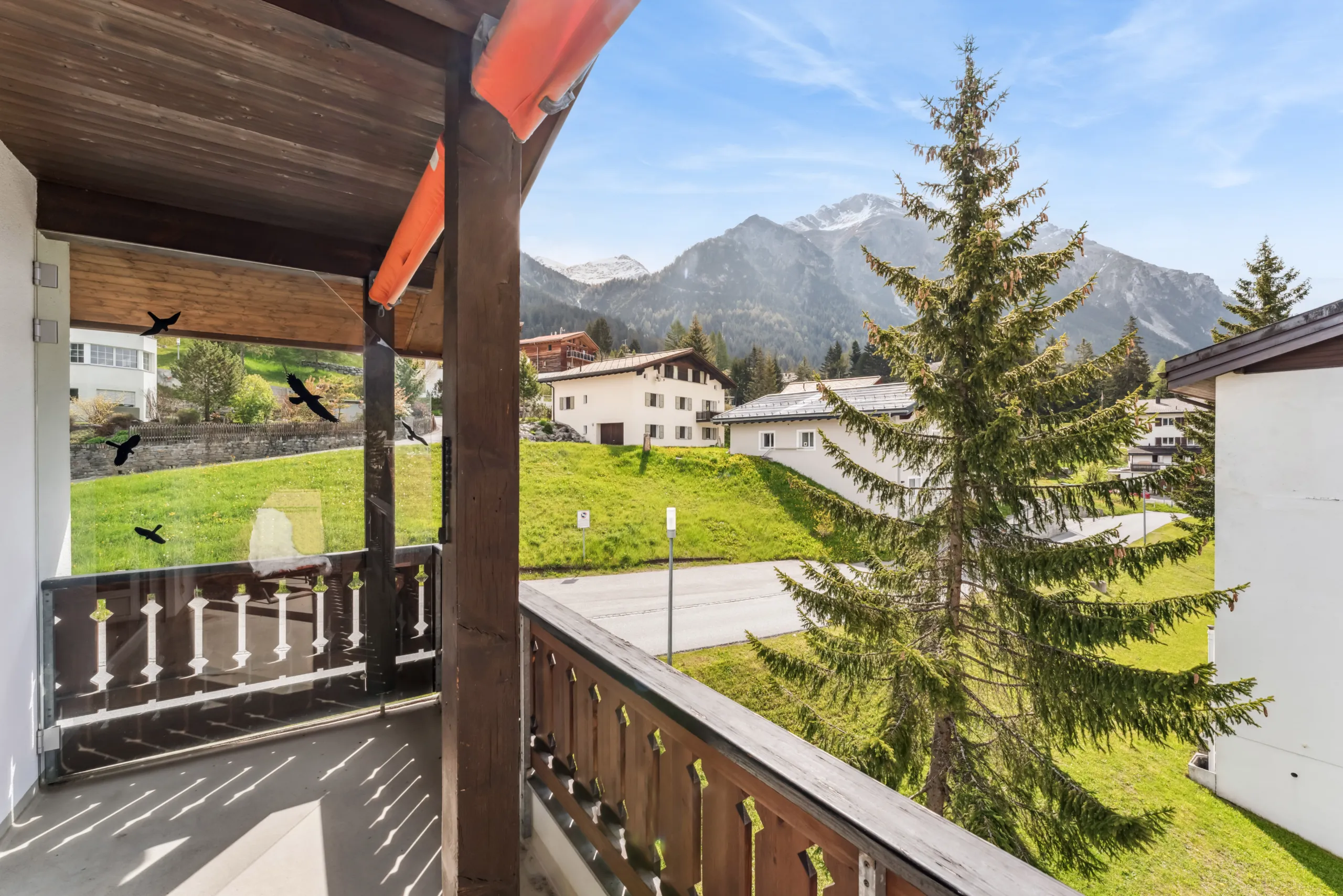 Gedeckter Holzbalkon mit Blick auf Tannen, Chalets und Berggipfel in Lenzerheide.