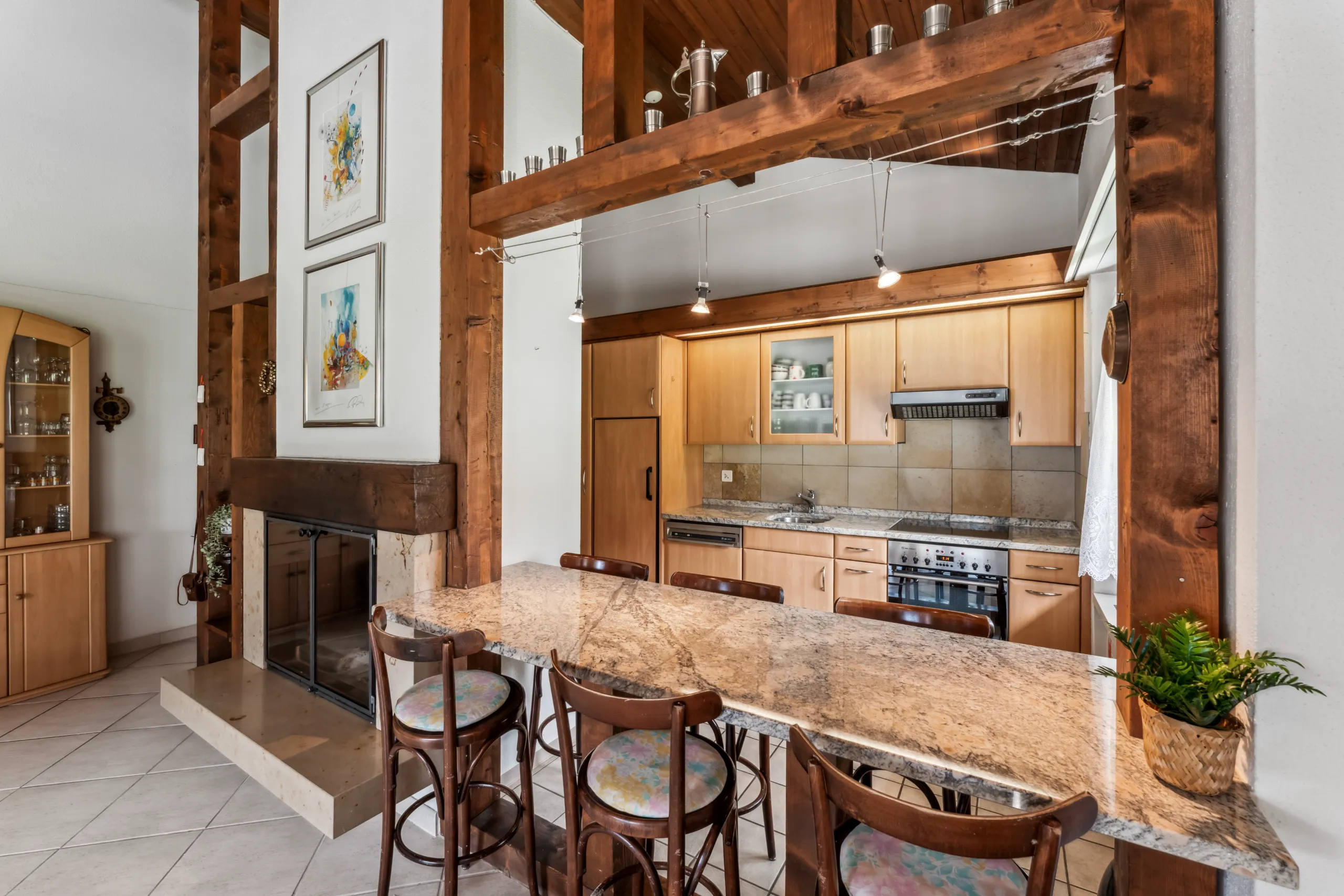 Offene Küche mit Granit-Essbar, Barhockern, Holzbalken und Cheminée in Wohnung in Lenzerheide