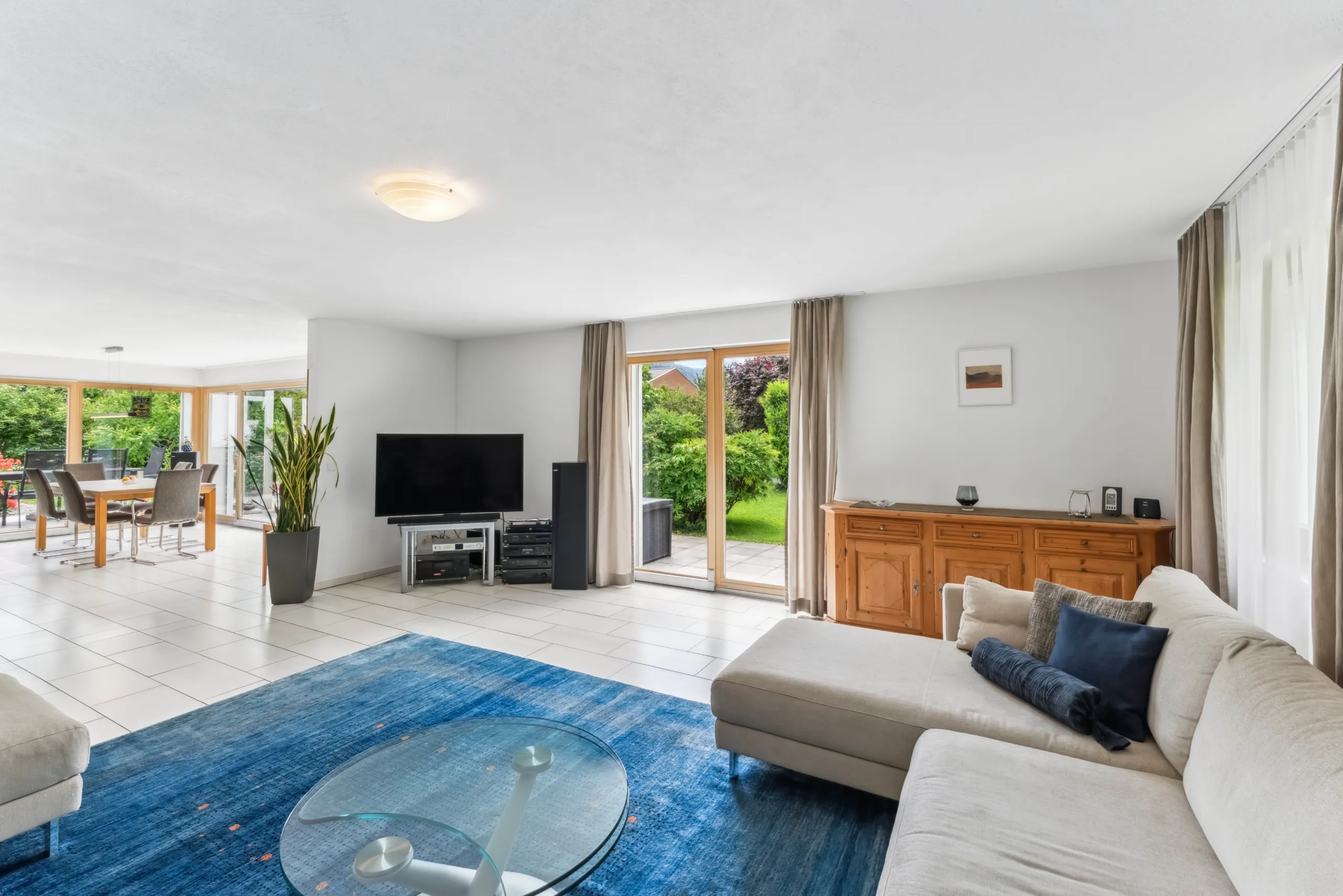 Helles Wohnzimmer mit Ecksofa, blauem Teppich und Fenstertür zum Garten