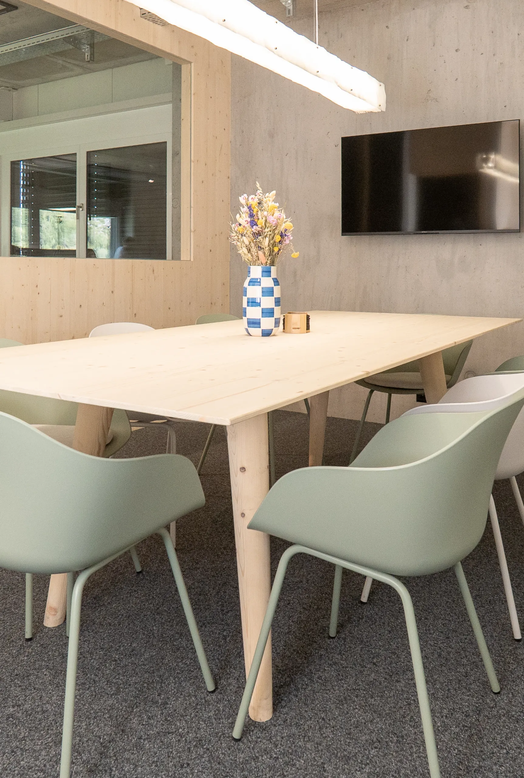 Moderner Besprechungsraum mit grossem Holztisch, mintgrünen Stühlen, Sichtbetonwand und integrierter Holzverkleidung.