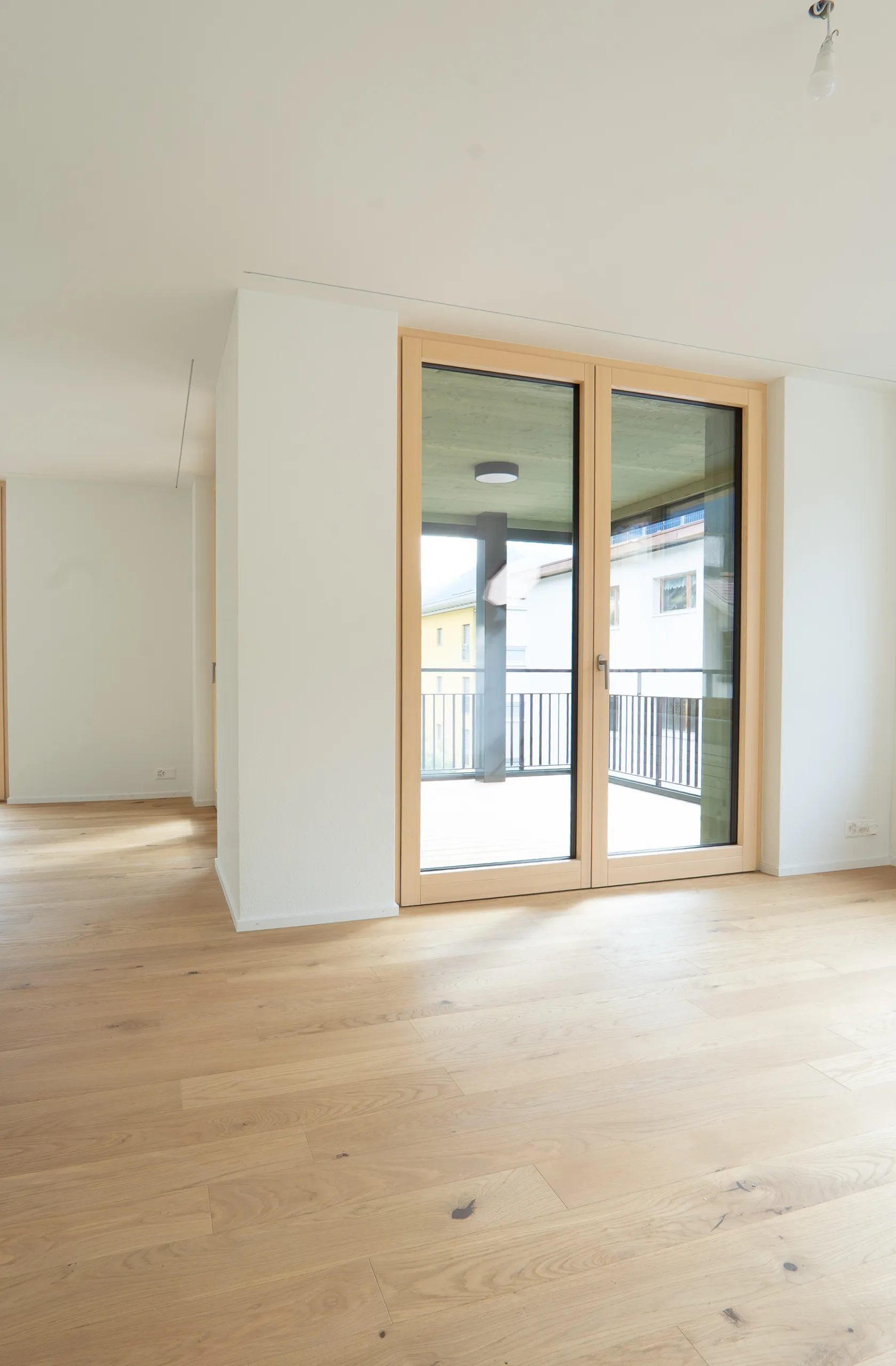 Grosszügiger Wohnbereich mit hellem Eichenparkett, weissen Wänden und bodentiefen Holzfenstertüren zur Terrasse.
