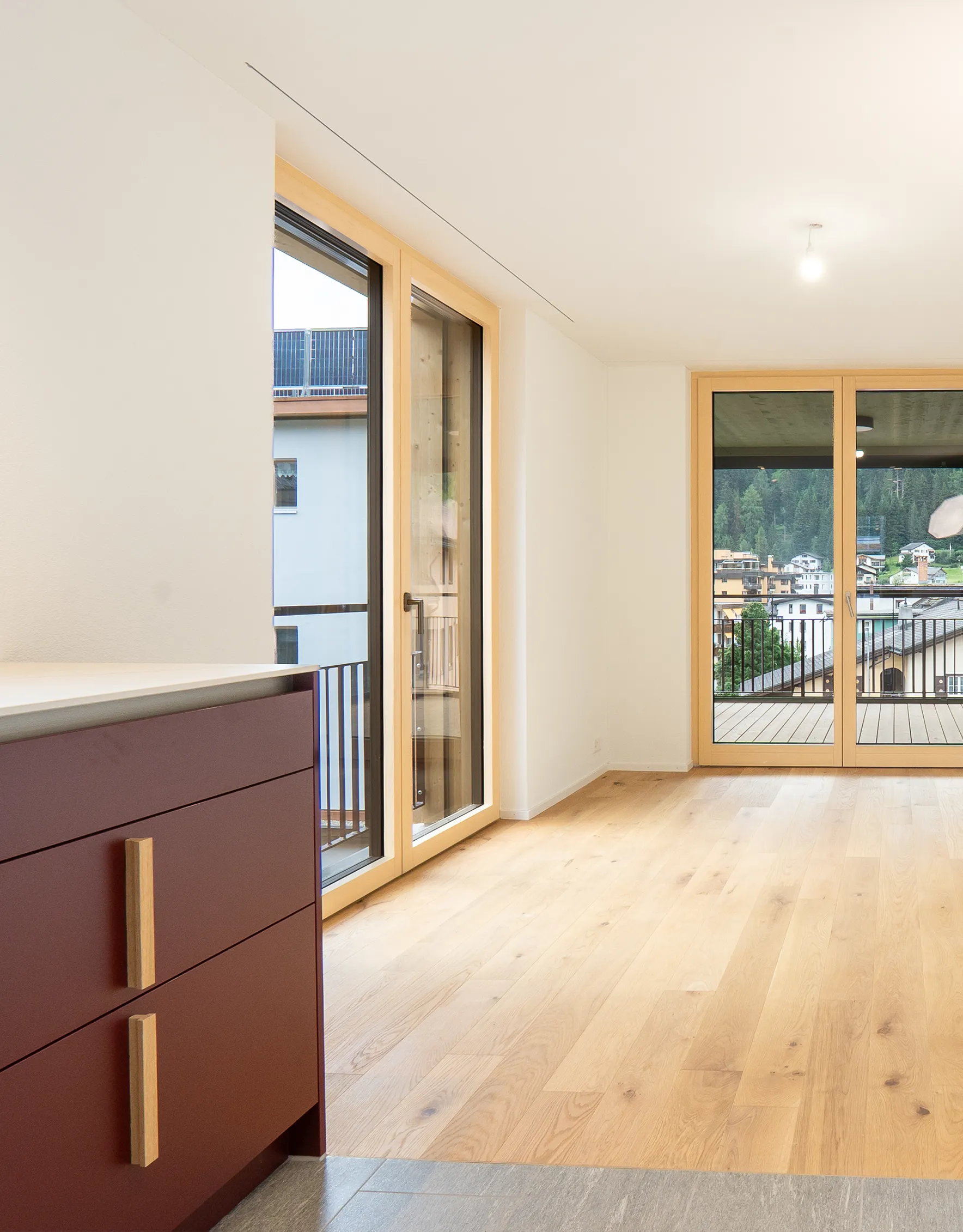 Moderner Wohnbereich mit hellem Eichenparkett, grossen Holzfenstern und Blick auf die Bündner Berglandschaft.