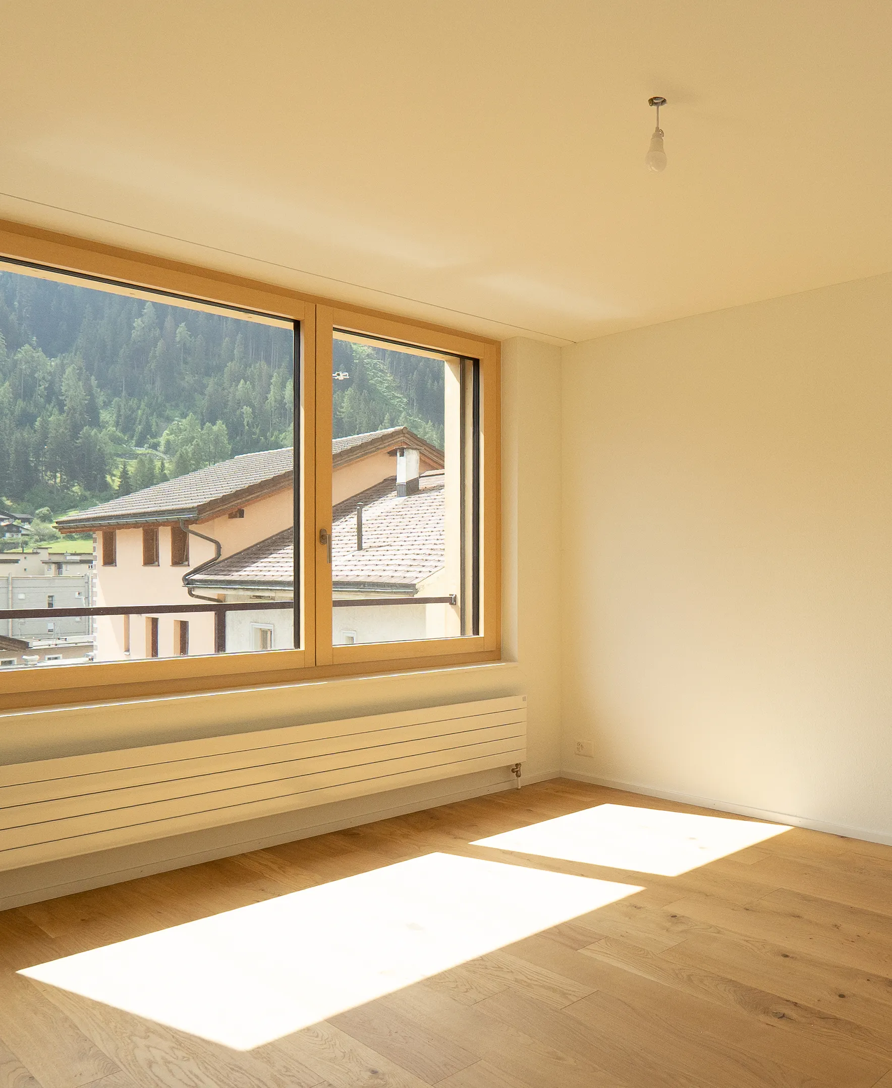 mittel-hoch-4 Sonniger Wohnraum mit Eichenparkett, grossen Holzfenstern und Blick auf die grüne Berglandschaft.