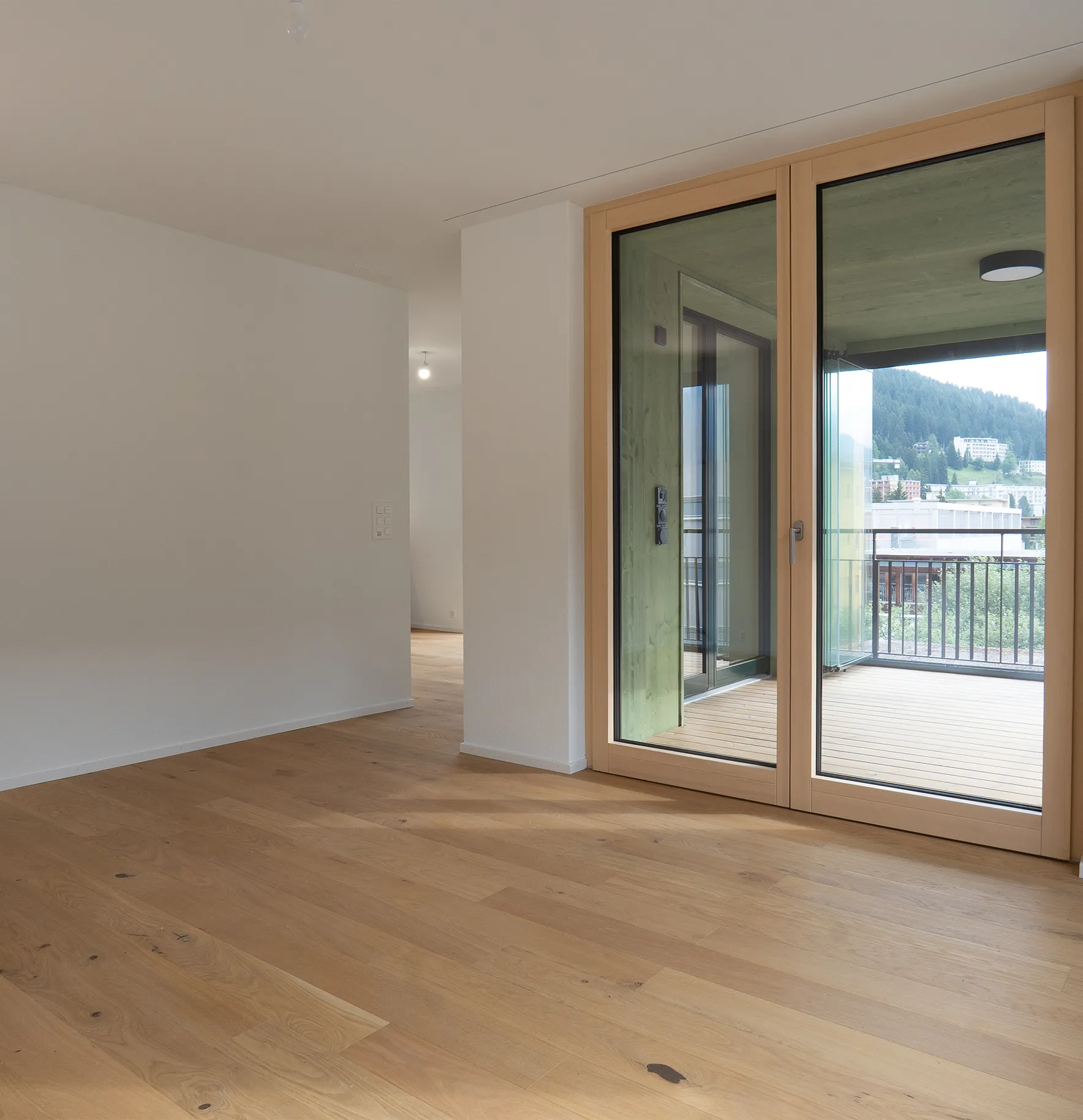 Heller Wohnraum mit Eichenparkett, weissen Wänden und grossen Holzfenstertüren zum überdachten Balkon.