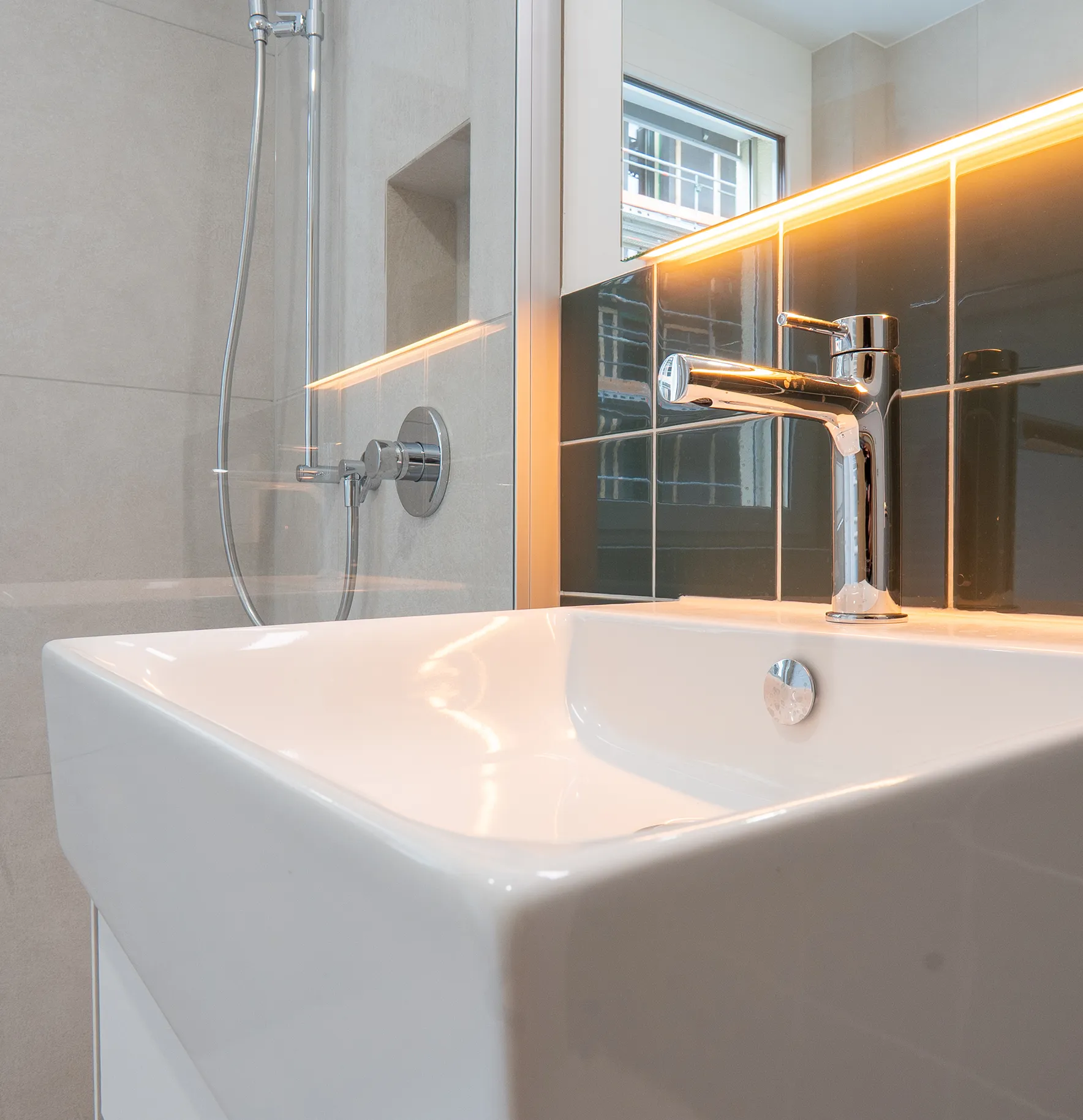 mittel-tief-5 Modernes Badezimmer mit weissem Waschtisch, Chromarmatur, dunkelgrünen Wandfliesen und indirekter Beleuchtung.